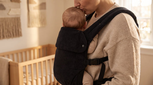 Baby zit hoog en strak in de zwarte corduroy draagzak van Laavir, met het gezichtje vrij